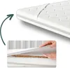 A close-up view of a mattress topper, showing its layered construction and a hand lifting a section to reveal the inner materials. Produktbild-Vorschau