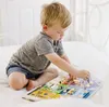 A young boy is sitting on a white bed and playing with a colorful toy board game. Produktbild-Vorschau