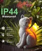 A solar-powered cat figurine with a butterfly on its back, placed in a garden setting with rain falling. Produktbild-Vorschau