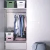An organized closet with clothes hanging on a rack and storage bins on shelves. Anteprima dell’immagine prodotto