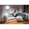 A woman sits on a couch in a living room, holding a smartphone. Produktbild-Vorschau