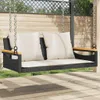 A black rattan swing bench with beige cushions is shown outdoors on a wooden deck, with a wooden fence and greenery in the background. Náhled obrázku produktu