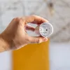 A hand holding a smart plug with a blurred background. Produktbild-Vorschau