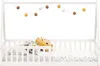 A white wooden children's bed with a mattress and bedding, decorated with a string of decorative balls. Produktbild-Vorschau
