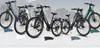 A lineup of electric bikes on a white and gray gradient background with a blurred city skyline in the distance. Voir les images du produit