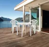 A white plastic table and chairs set on a wooden deck overlooking a lake and mountains. Voir les images du produit