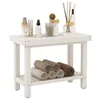 A white wooden shower bench with bathroom accessories on top and rolled towels on the shelf below. Podgląd zdjęcia produktu