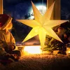 A child in a Santa hat looks out a window at a snowy night scene with a large illuminated star decoration. Produktbild-Vorschau