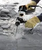A person wearing work gloves is using a WORX WX339 Bohrhammer to break apart stone tiles. Náhled obrázku produktu