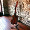 A guitar on a stand in front of a stone wall. Náhľad obrázku produktu