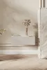 A modern bedroom scene featuring a white floating nightstand with a ribbed texture, holding a vase of dried flowers and two books. The wall has a textured finish and soft lighting. Náhled obrázku produktu