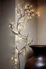 A decorative illuminated branch with warm white lights is mounted on a wall next to a large brown vase. Produktbild-Vorschau