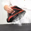 A person is holding a black and red steam iron over a dark gray fabric. Voir les images du produit