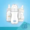 Three baby bottles are displayed against a light blue background, with a graphic of stacked dishes in the lower right corner. Náhled obrázku produktu
