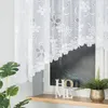 A white lace curtain with a floral pattern hangs in front of a window. A plant and decorative letters spelling 'HOME' are on the windowsill. Náhled obrázku produktu