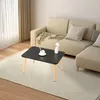 A small black coffee table with wooden legs sits on a rug in front of a beige sectional sofa. Produktbild-Vorschau