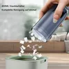 A hand is shown emptying a handheld vacuum cleaner into a trash bin, with paper scraps falling out. Produktbild-Vorschau