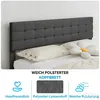 A close-up view of a dark gray upholstered headboard on a bed with beige pillows and a flower-shaped pillow. Produktbild-Vorschau