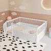 A white wooden crib with a door and a ramp is set up in a child's room with pink walls and cloud decorations.