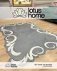 A rug with a decorative border is laid out on a wooden floor, with a sofa and artwork visible in the background. The brand logo is also displayed. Produktbild-Vorschau