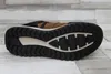 The sole of a brown and black sneaker is shown against a light gray and white wood-plank background. Voir les images du produit
