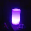 A cylindrical LED lamp is lit with purple light, placed on a book with a remote control next to it. Produktbild-Vorschau