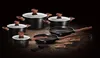 A collection of black cookware with wooden handles and lids, arranged on a dark wooden surface against a black background. Produktbild-Vorschau