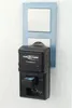A black Ansmann Powerline 2 battery charger is plugged into a wall socket, with a small blue adapter inserted into one of its ports. Produktbild-Vorschau
