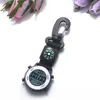 A digital watch with a compass attached, set against a white background with blurred flowers in the upper left and upper right corners. Produktbild-Vorschau