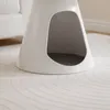 A close-up view of a modern, white, cone-shaped pet bed with a gray cushion inside, placed on a light-colored rug with a subtle circular pattern. Produktbild-Vorschau