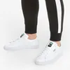 A close-up shot of a person's legs wearing black Puma sweatpants and white Puma sneakers. Produktbild-Vorschau