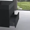 A black vanity cabinet with an open drawer, set against a bright, modern interior with a large window overlooking a garden. Produktbild-Vorschau