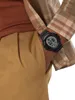 A close-up shot of a person's wrist wearing a digital watch, with part of their plaid shirt and pants visible. Náhled obrázku produktu