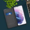 A smartphone with a flip case is placed on a dark blue surface, with a laptop and green leaves in the background. Náhled obrázku produktu
