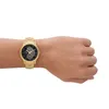 A person's wrist wearing a gold watch with a black face. Voir les images du produit