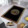 A black rug with a gold Versace-like pattern is placed on a light-colored floor in a room with gray chairs and a radiator. Produktbild-Vorschau