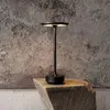 A black LED table lamp is placed on a wooden block against a textured gray wall. Produktbild-Vorschau