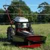 A rotary mower is parked in a grassy field with trees and a fence in the background. Produktbild-Vorschau