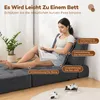 A woman is sitting on a dark gray floor sofa, reading a book. The sofa is shown in a reclined position, with labels indicating support for the back, spine, hips, and legs. Náhled obrázku produktu