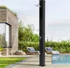An outdoor shower is set up on a wooden deck next to a pool, with lounge chairs and a modern building in the background. Produktbild-Vorschau
