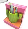 A green ceramic cactus-shaped pen holder with colorful pencils and a ruler inside, displayed in its pink and orange packaging. Voir les images du produit