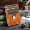 A wooden kalimba instrument is placed on a textured surface, with books and a pocket watch in the background. Produktbild-Vorschau