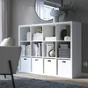 A white IKEA Kallax shelving unit filled with books and decorative items, placed in a living room setting. Produktbild-Vorschau