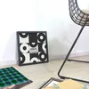 A framed vinyl record art piece is displayed leaning against a white wall, with a patterned mat and an open frame on the floor. Podgląd zdjęcia produktu