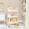A white three-tier rolling cart filled with stuffed animals and toys, placed in a room with a white cabinet and a framed picture on the wall. Náhled obrázku produktu