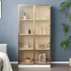 A tall, narrow glass display cabinet with gold trim, filled with decorative items and books, placed in a room with a blue wall and a grey sofa. Náhľad obrázku produktu