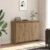 A wooden sideboard with three doors is placed against a wall, with a plant on the left and a sofa on the right. A framed picture hangs on the wall above the sideboard. Náhľad obrázku produktu