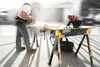 A man is using a circular saw to cut a piece of wood on a portable work table. Anteprima dell’immagine prodotto