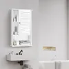 A white bathroom cabinet with an open shelf and a louvered door is mounted on a textured gray wall above a white sink. The cabinet contains toiletries and folded towels. A bathtub is visible in the background. Náhled obrázku produktu