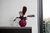A plant in a purple pot sits on a gray surface next to two glass vases. Anteprima dell’immagine prodotto
